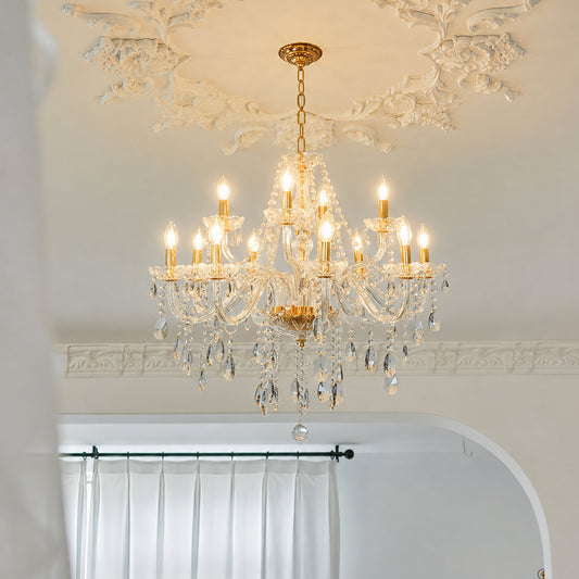 A multi-light crystal chandelier with gold-toned metal arms and hanging clear glass prisms, suspended from a decorative white ceiling in an elegant interior.