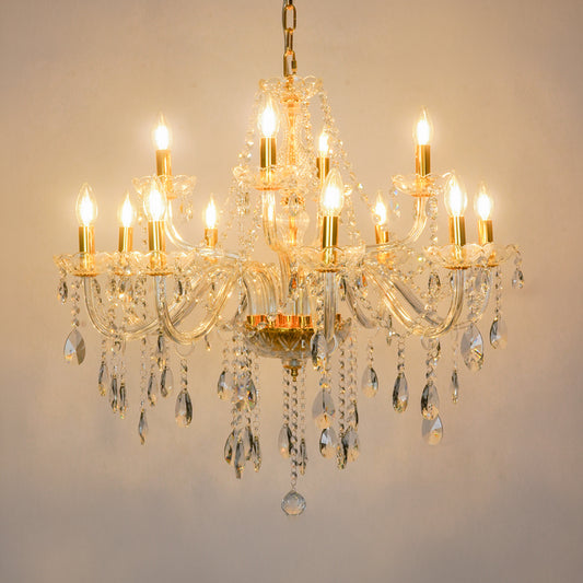A multi-arm crystal chandelier with gold-toned metal arms and clear hanging teardrop prisms, shown illuminated against a plain light beige wall.
