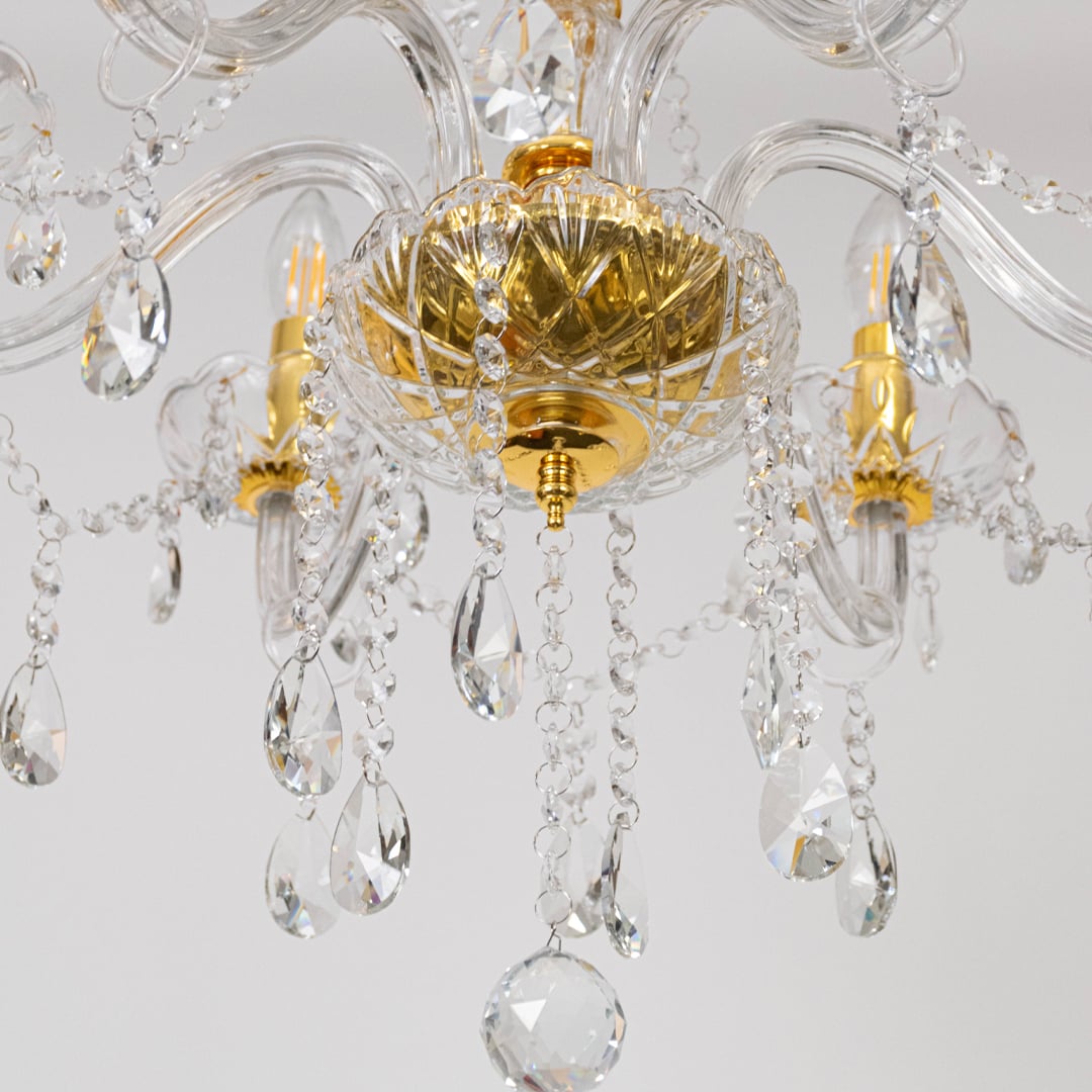 Closeup of gold chandelier showing crystal detailing glass arms and candle style bulbs for luxury ceiling decor.