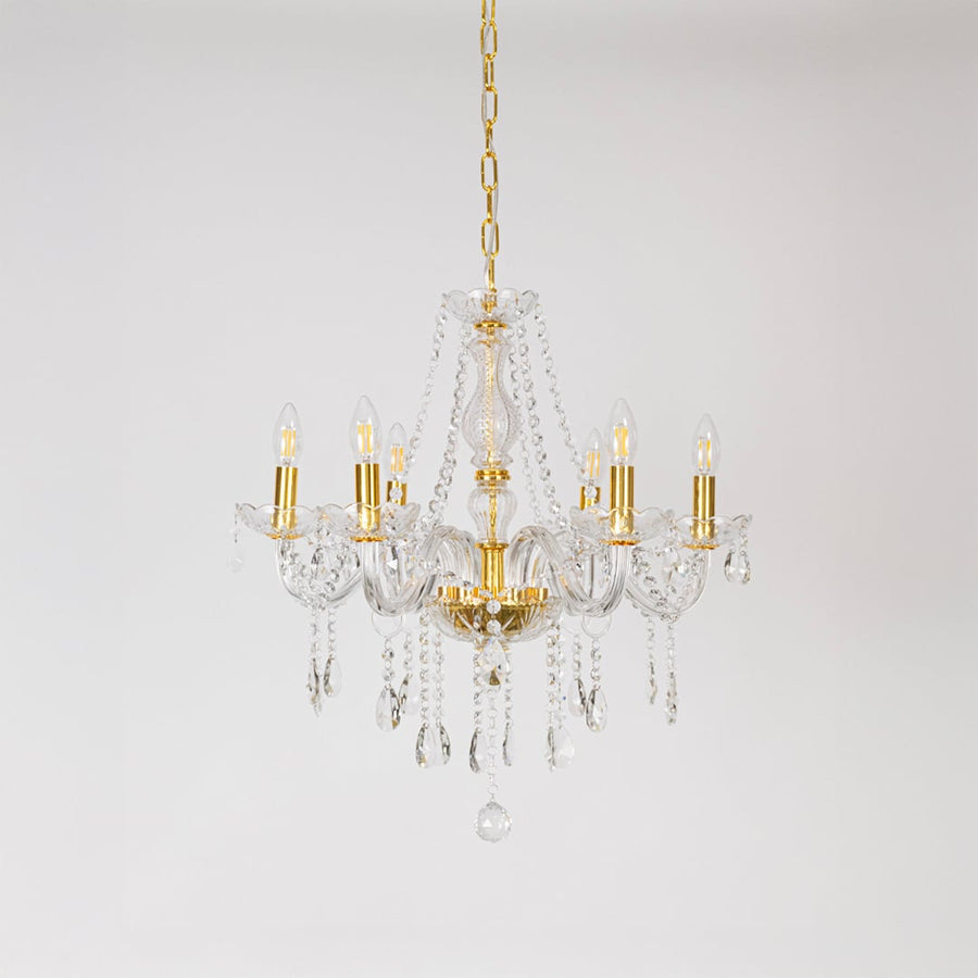 Gold chandelier with lights off featuring crystal accents and glass frame on plain white background.