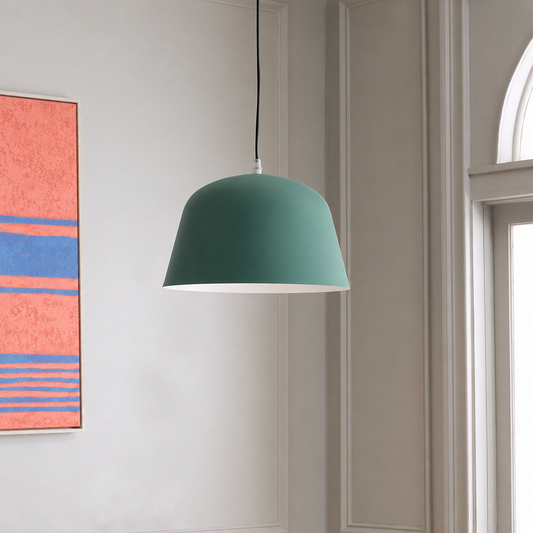 A modern dome-shaped pendant light in a muted teal green shade with a white interior, hanging from a black cord in a bright room with paneled walls and a colorful abstract painting.