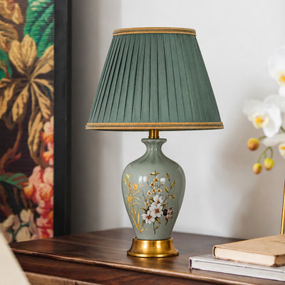 Vintage sage green ceramic table lamp with floral print and pleated fabric shade on wooden side table for living room decor.