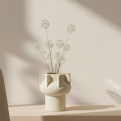 Beige textured ceramic decorative vase styled with delicate flowers on console table in warm modern interior setting.