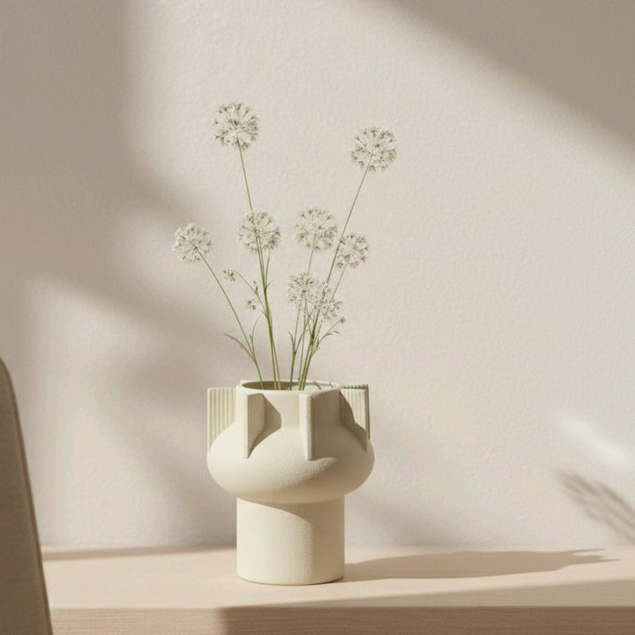 Beige textured ceramic decorative vase styled with delicate flowers on console table in warm modern interior setting.