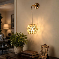 Ornate gold brass geometric cage ball wall sconce light casting warm shadows on living room wall for luxury interior decor.