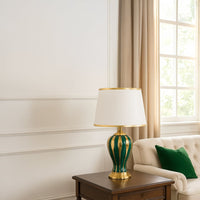 Table lamp with green and gold ceramic base and white shade styled for elegant modern home decor on a classic console.