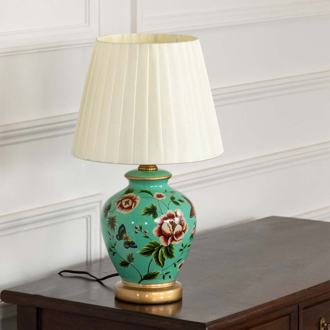 Green floral ceramic table lamp with white shade displayed on white background with lights off.