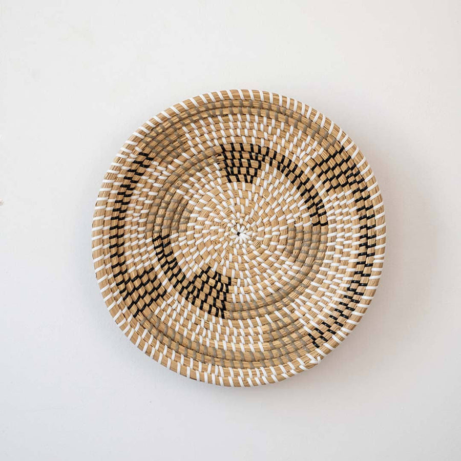 Handwoven seagrass round wall basket decor in natural beige with black geometric pattern displayed on white background.