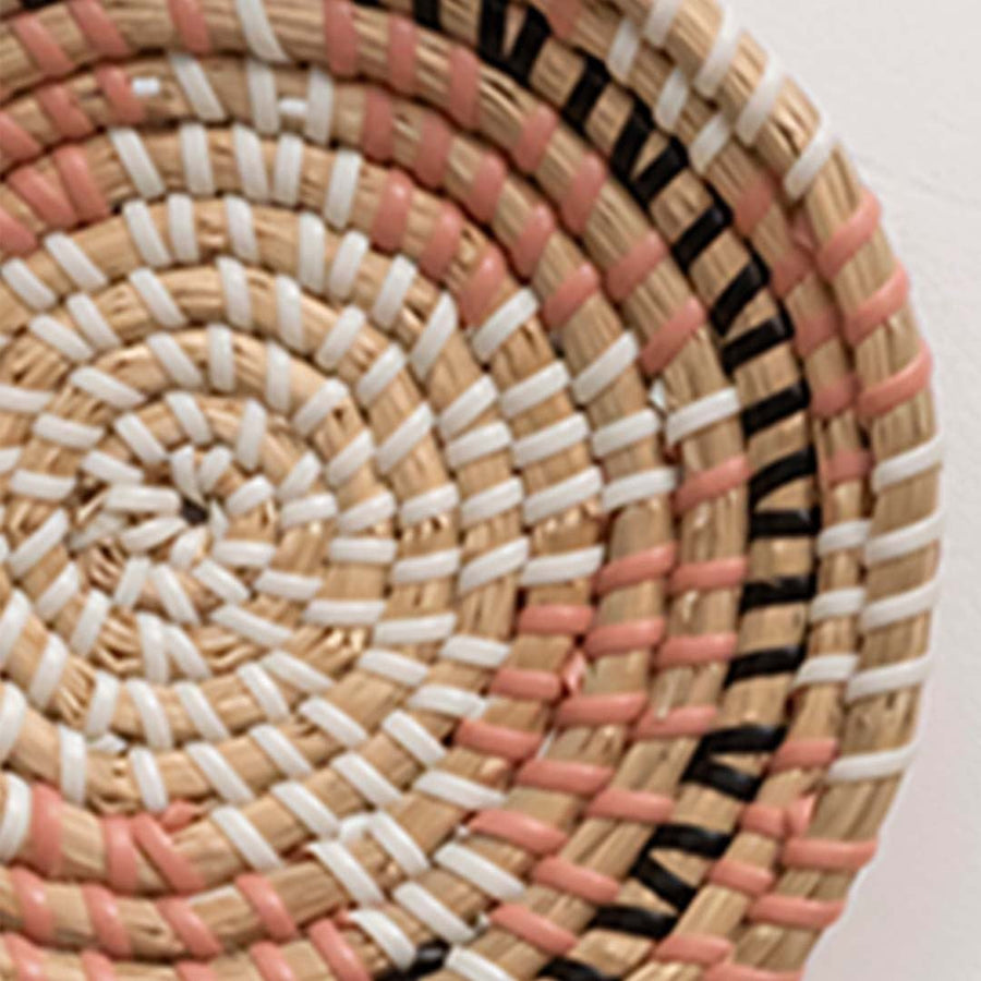 Closeup of handwoven wicker basket wall decor showing detailed natural beige pink and black woven pattern design.