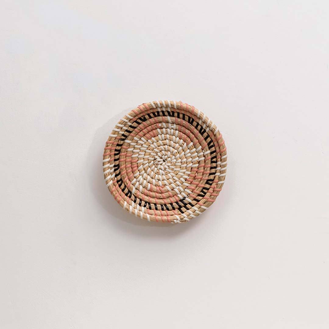 Handwoven seagrass round wall basket decor in natural beige with coral woven center displayed on white background.