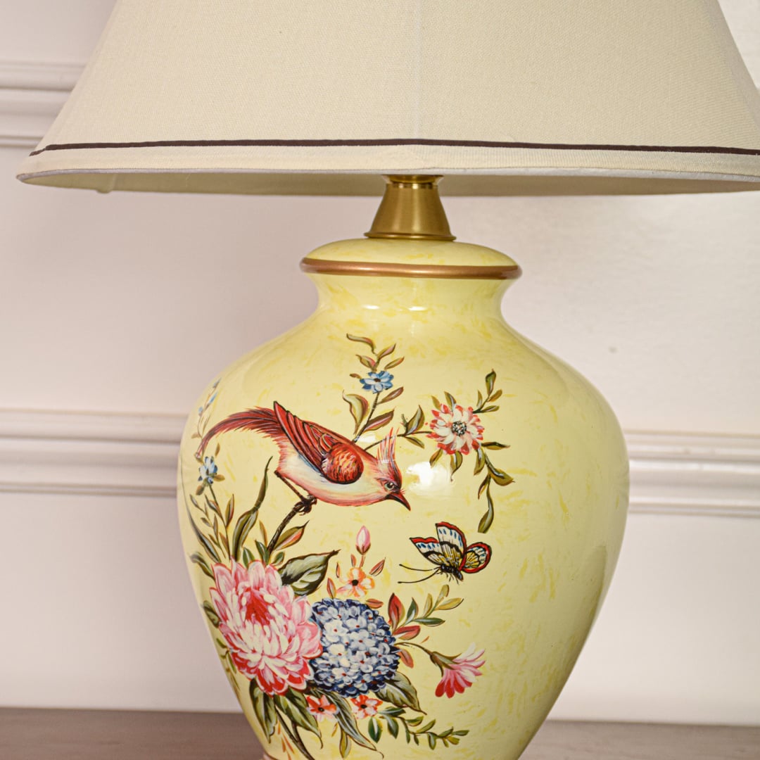 Closeup of yellow ceramic table lamp highlighting detailed floral bird artwork smooth glazed surface and gold metal base.