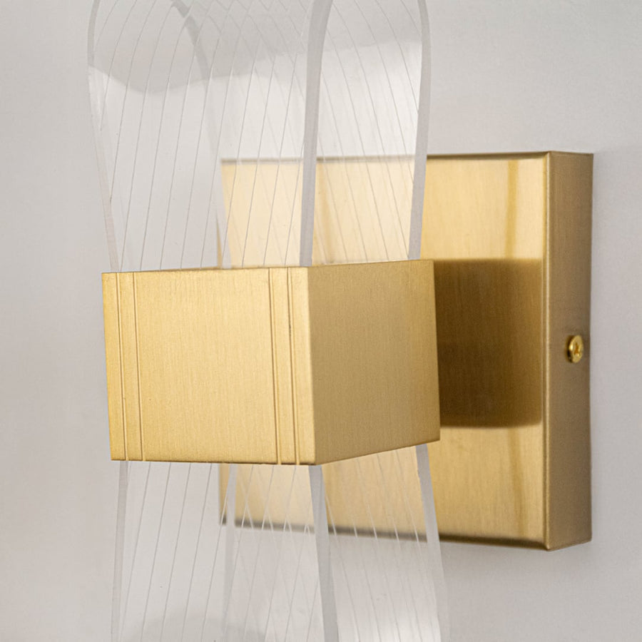 Closeup of gold metal wall light with ribbed clear glass shade highlighting elegant curved shape and fine detailing.