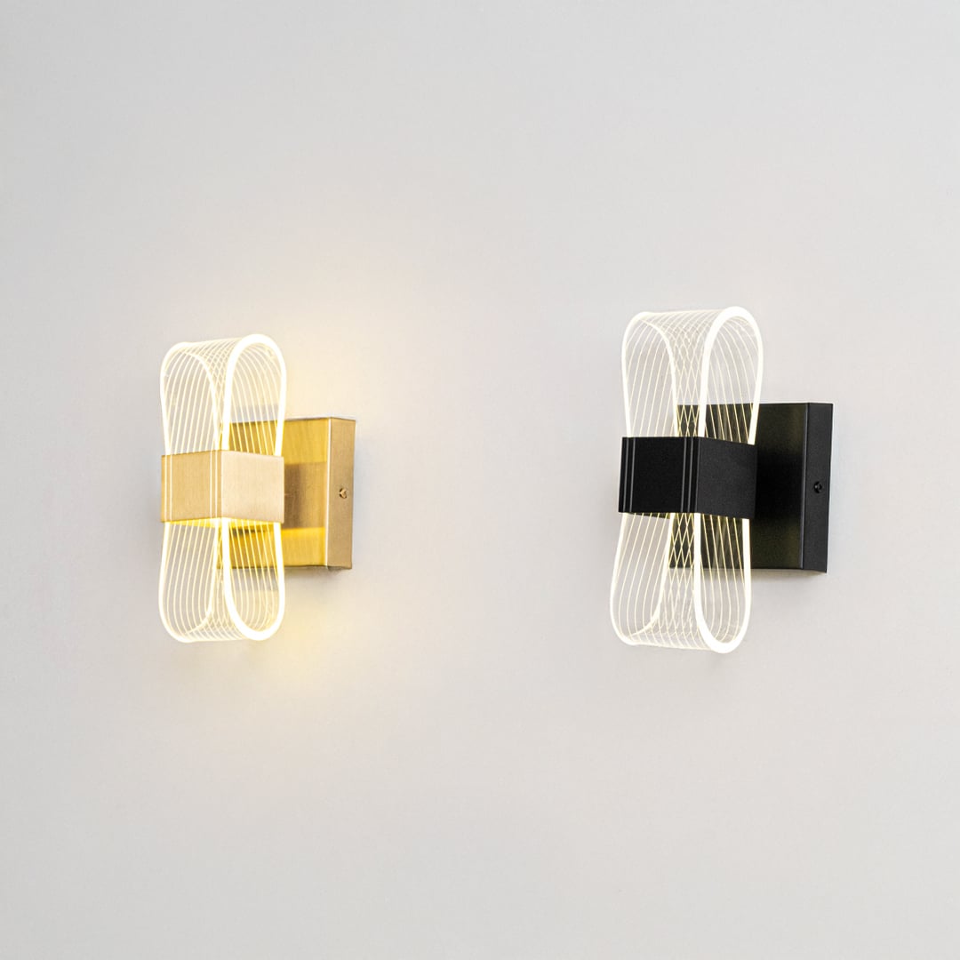 Gold wall lights with ribbed clear glass shades illuminated on a clean white background showing bright warm glow.