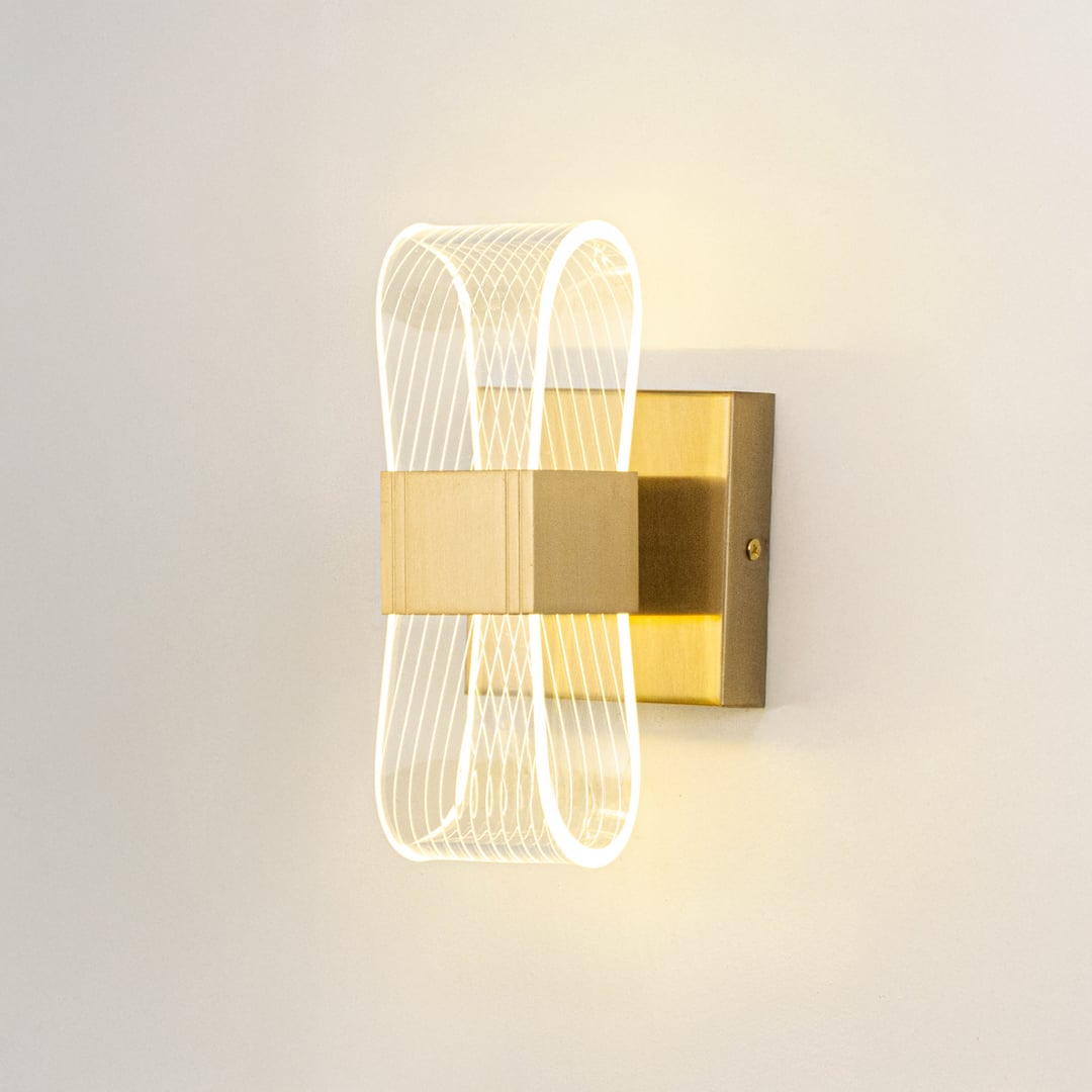Gold wall light with ribbed clear glass shade illuminated on a clean white background for clear bright visibility.
