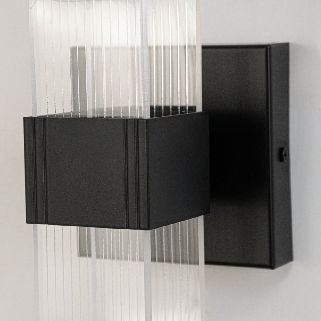 Closeup of black wall light with ribbed clear glass shade highlighting smooth texture and elegant curved design.