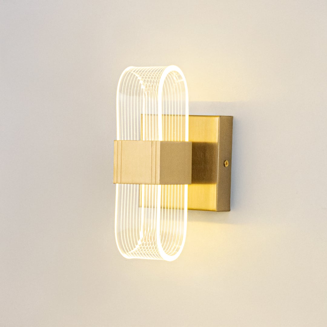 Gold wall light with ribbed clear glass shade illuminated on a clean white background for clear visibility.