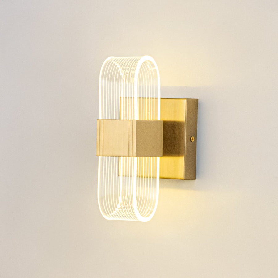 Gold wall light with ribbed clear glass shade illuminated on a clean white background for clear visibility.