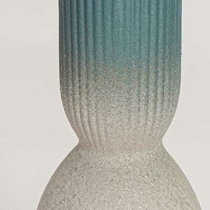 Closeup of beige ceramic vase with textured finish and glossy blue top ideal for elegant home decor shelf styling.