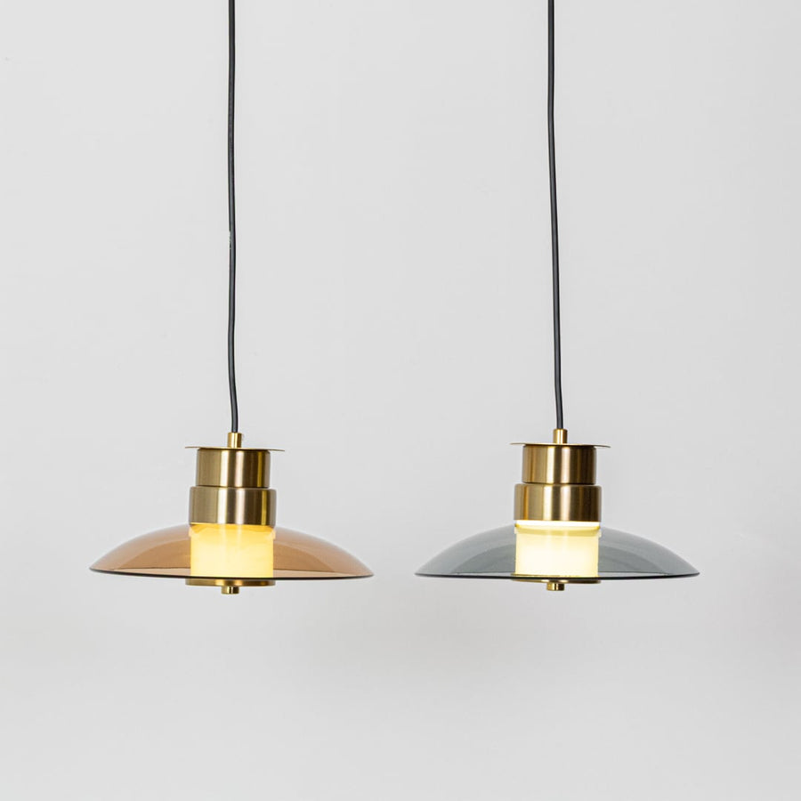 Amber and smoke grey glass pendant lights with gold metal tops shown with lights on side by side highlighting warm modern illumination.