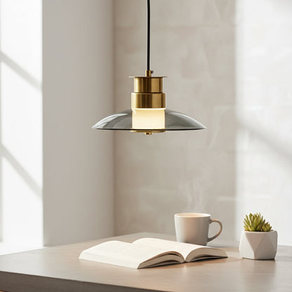 A modern pendant light with a gold and smoked glass shade glowing warmly above an open book and coffee cup in a bright peaceful reading corner.