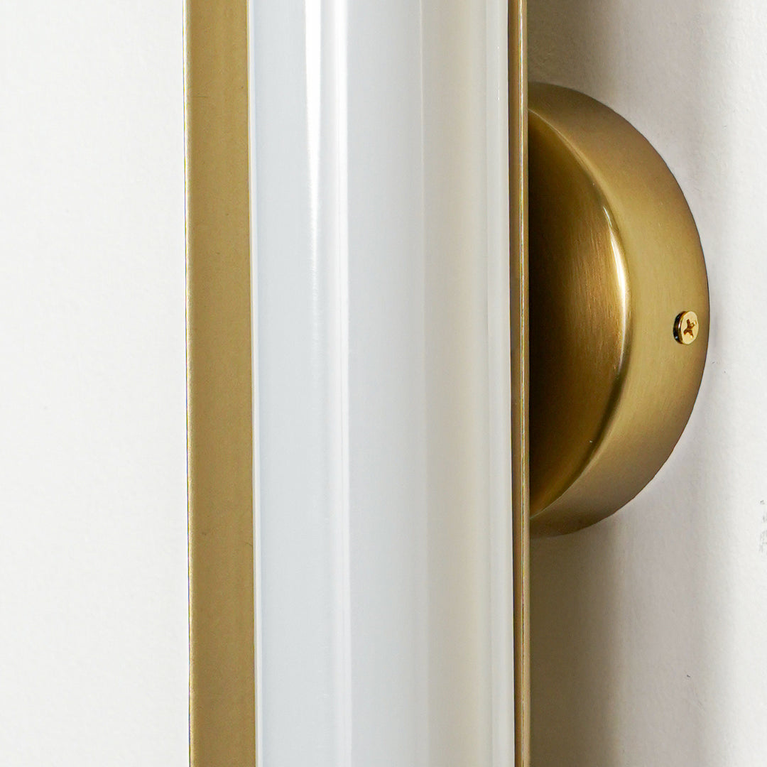 Close view of gold wall light with vertical frosted glass tube mounted on neutral wall background showcasing modern premium lighting design.
