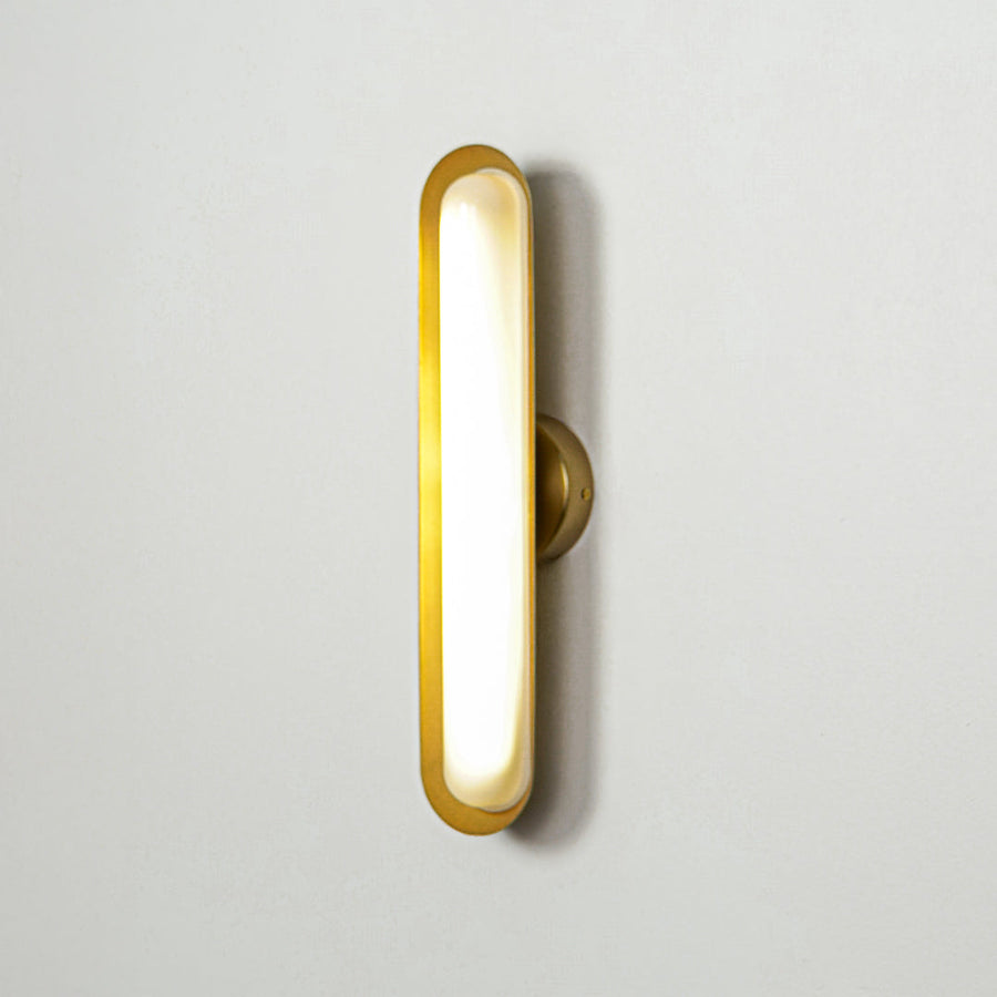 Contemporary gold wall sconce with glowing oval shape on clean wall background ideal for stylish interior accent lighting.
