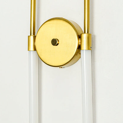 Modern gold wall sconce with round backplate and dual glass tube shades on clean wall background perfect for contemporary interior decor lighting.