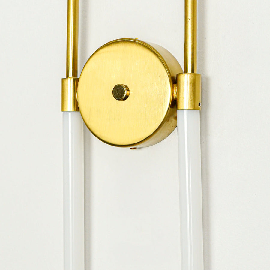 Modern gold wall sconce with round backplate and dual glass tube shades on clean wall background perfect for contemporary interior decor lighting.