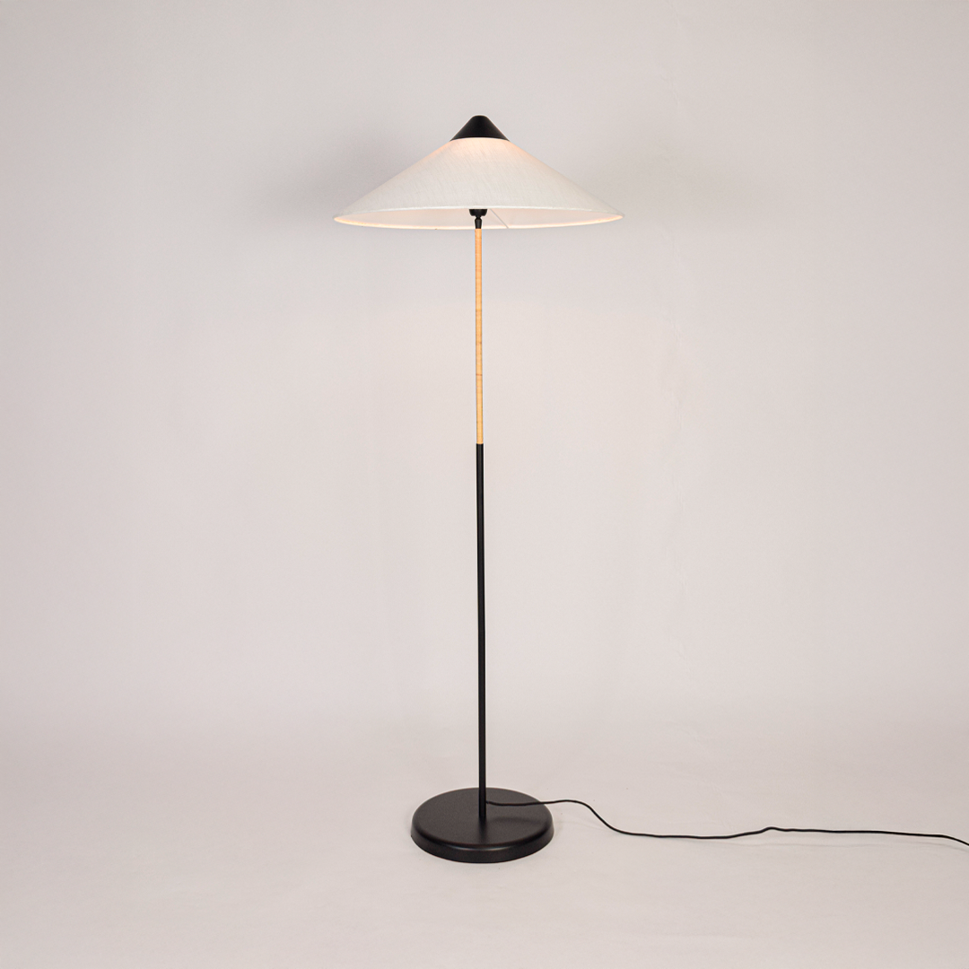 Floor lamp illuminated on clean white background showing tall sculpted base fabric drum shade and warm light output for modern home interiors.