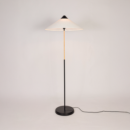 Floor lamp illuminated on clean white background showing tall sculpted base fabric drum shade and warm light output for modern home interiors.