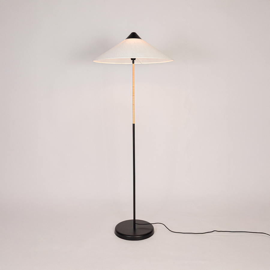 Floor lamp illuminated on clean white background showing tall sculpted base fabric drum shade and warm light output for modern home interiors.