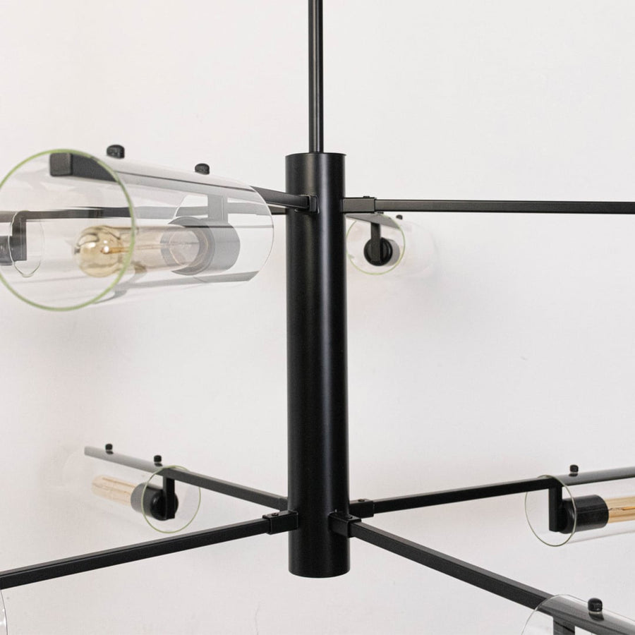 Detailed closeup of clear glass tube shade with exposed Edison bulb and black metal arms on contemporary chandelier fixture.