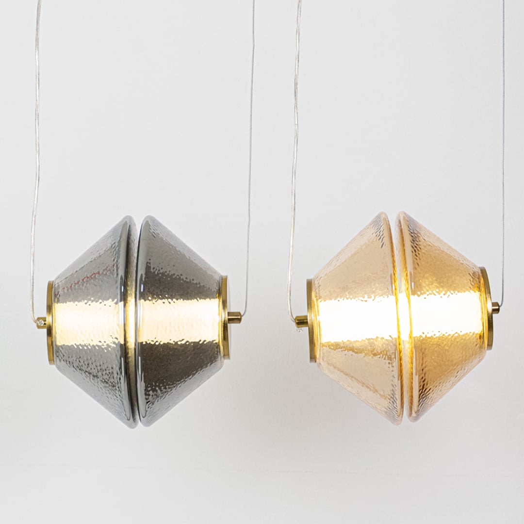 Two textured glass pendant lights shown side by side with the lights on highlighting amber and grey glass tones for a warm balanced glow.