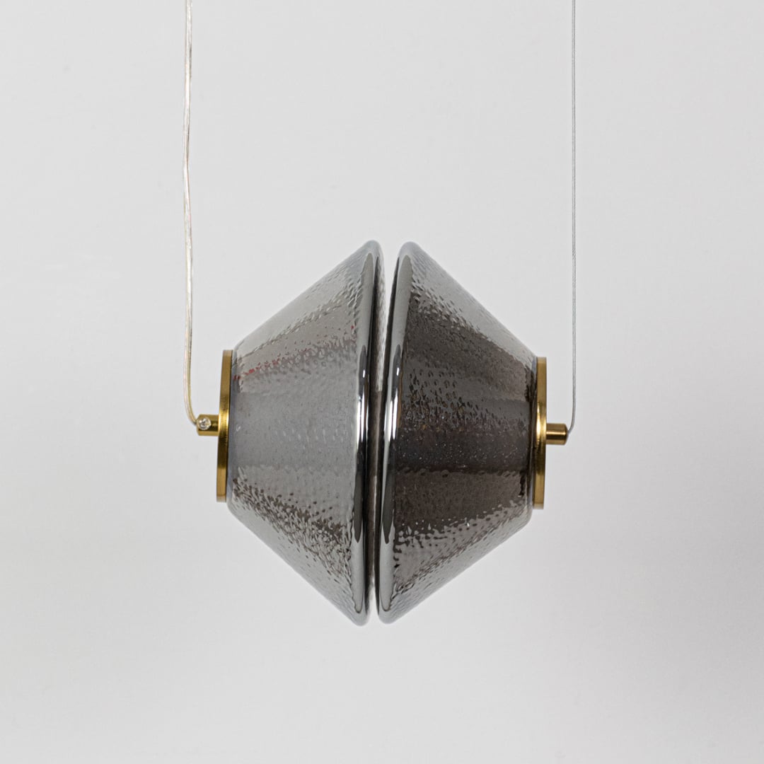 A hammered glass pendant light with golden details shown with the light off revealing the reflective textured grey glass surface.