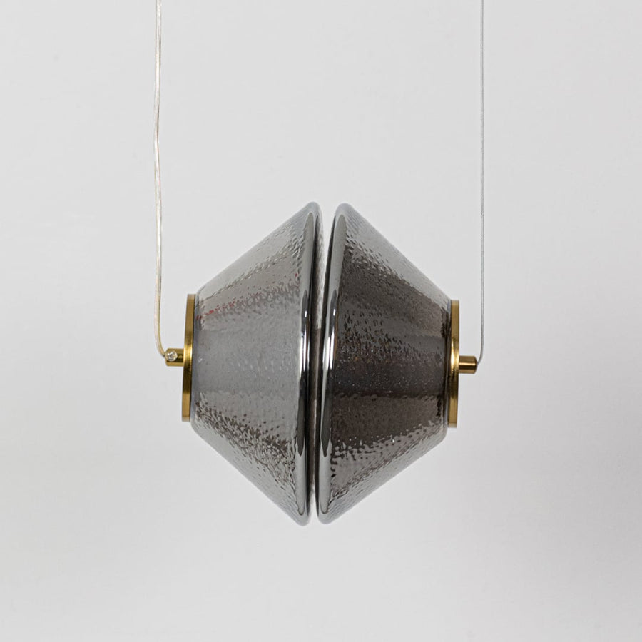 A hammered glass pendant light with golden details shown with the light off revealing the reflective textured grey glass surface.