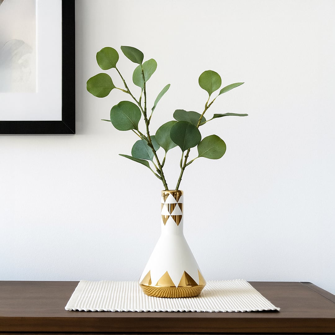 White ceramic vase with green leafy stems styled on table creating fresh minimal look for modern interior Decor.