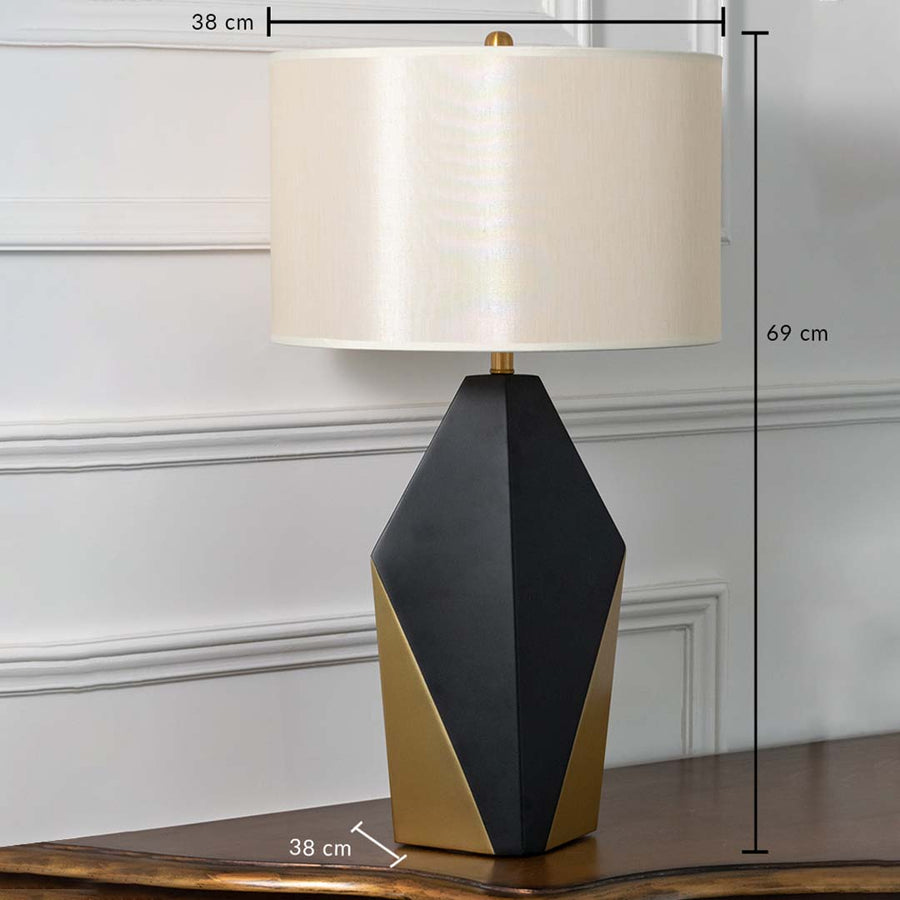 Black and gold geometric table lamp with white drum shade shown with dimensions of 38 cm width 69 cm height and 38 cm depth ideal for side tables or consoles.