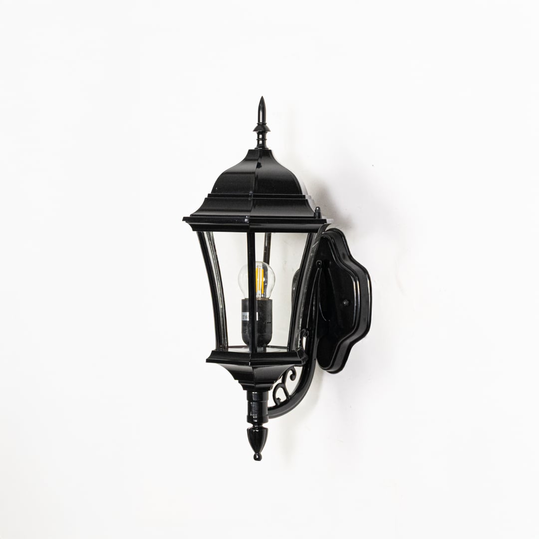 Traditional black metal outdoor wall lantern switched off on white background highlighting classic lantern shape and metal detailing.