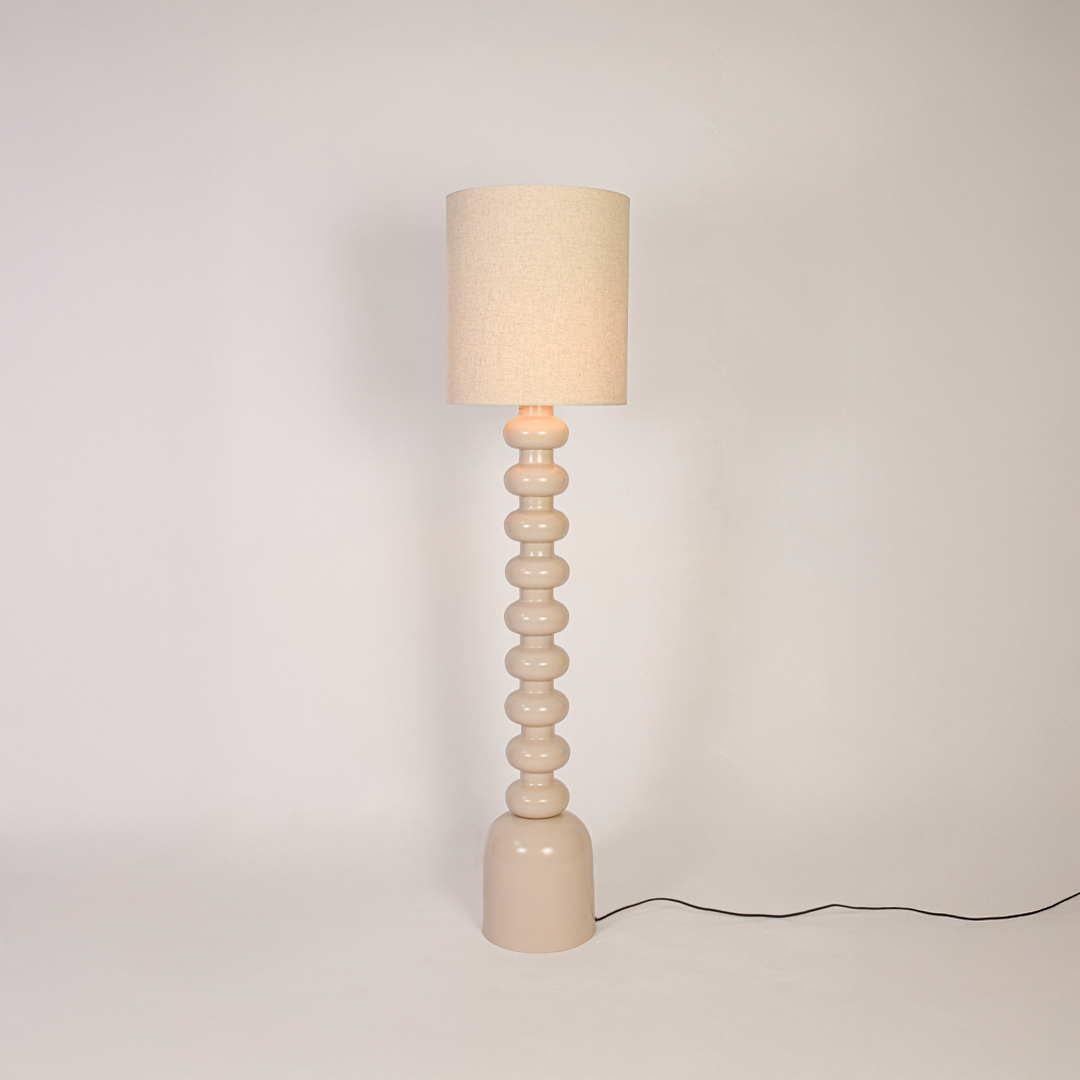 Floor lamp switched on on white background highlighting sculpted stacked base and fabric drum shade with soft light for minimalist home styling.