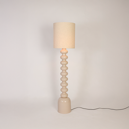 Floor lamp switched on on white background highlighting sculpted stacked base and fabric drum shade with soft light for minimalist home styling.
