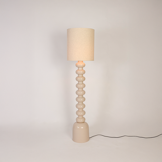 Floor lamp switched on on white background highlighting sculpted stacked base and fabric drum shade with soft light for minimalist home styling.