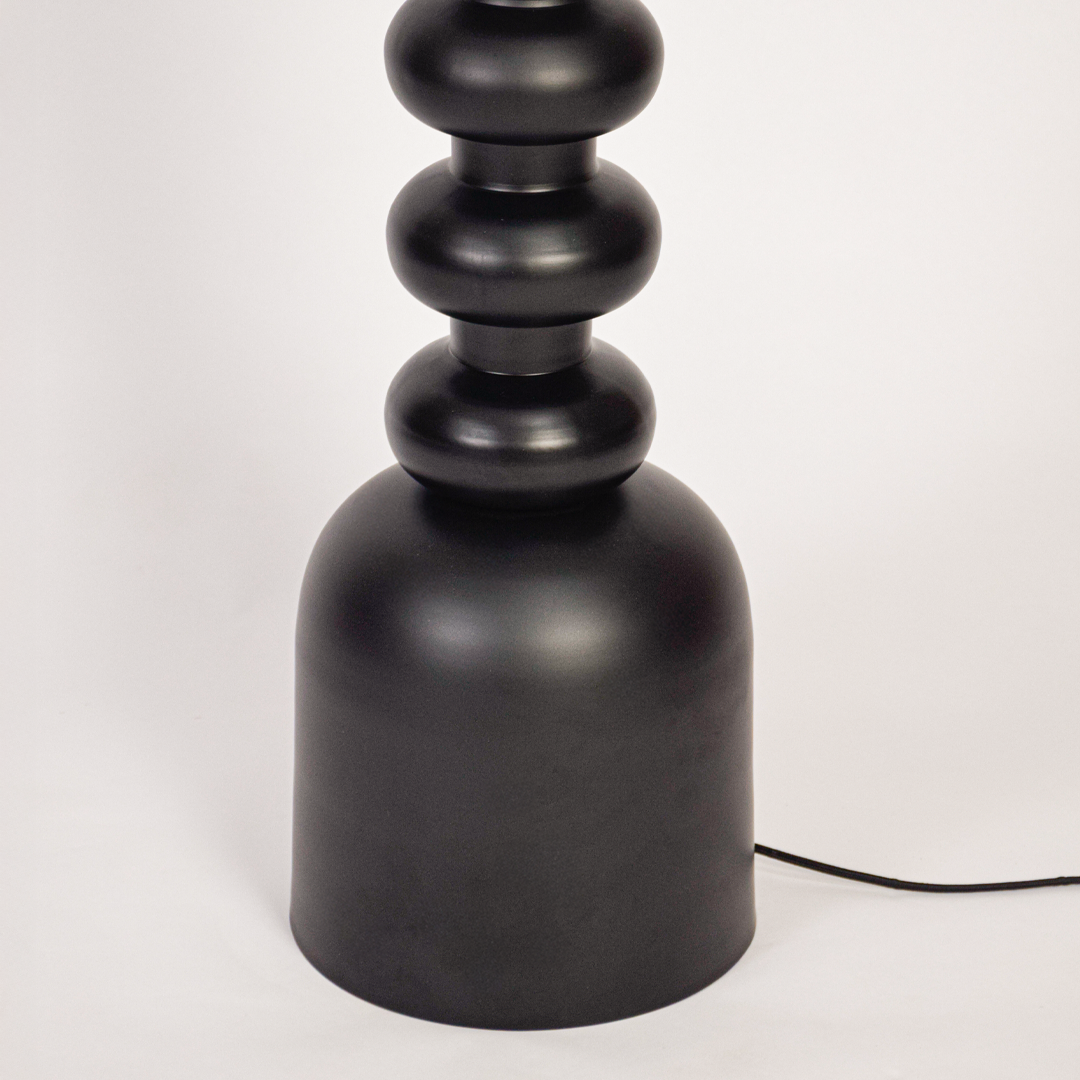 Floor lamp closeup showing textured black stacked base and fabric drum shade with warm bulb glow highlighting modern craftsmanship and premium finish.