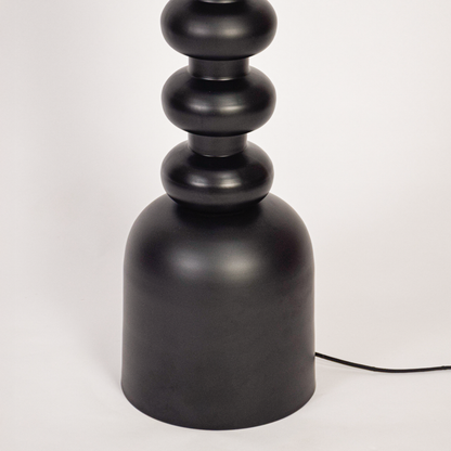 Floor lamp closeup showing textured black stacked base and fabric drum shade with warm bulb glow highlighting modern craftsmanship and premium finish.
