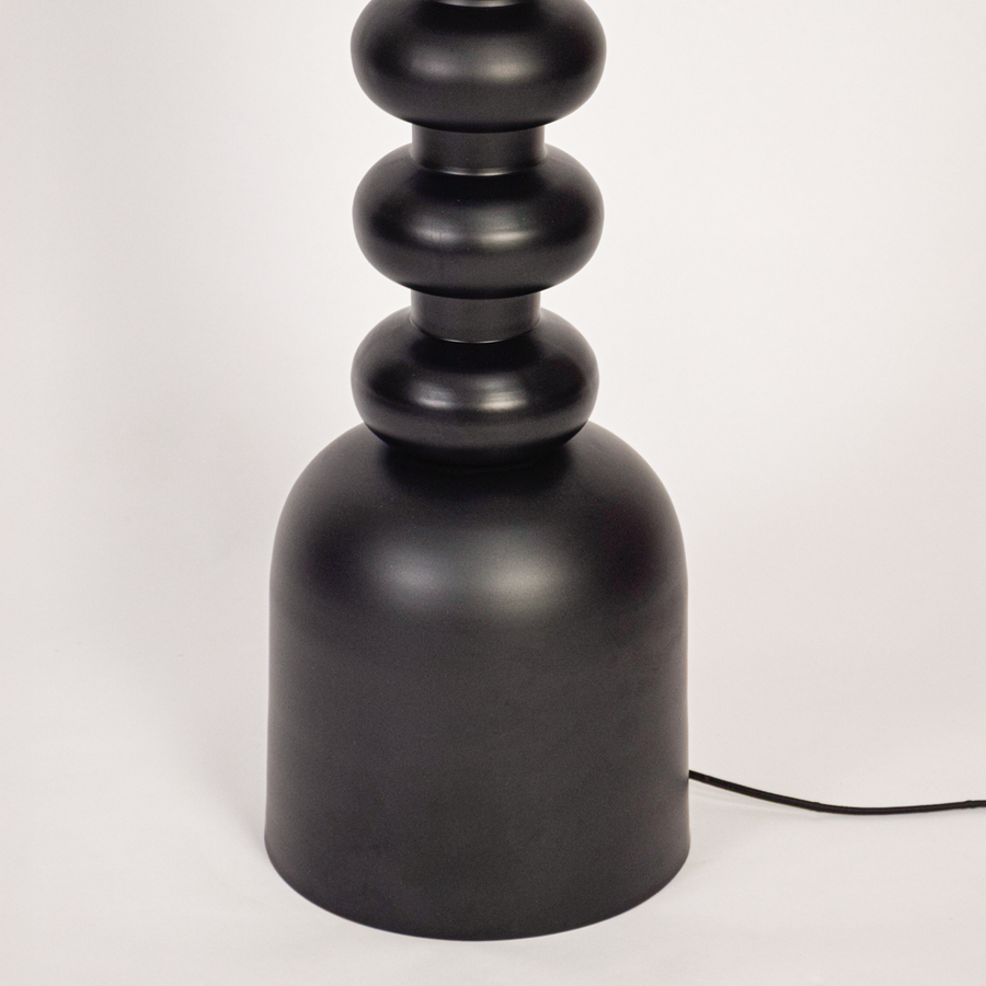 Floor lamp closeup showing textured black stacked base and fabric drum shade with warm bulb glow highlighting modern craftsmanship and premium finish.