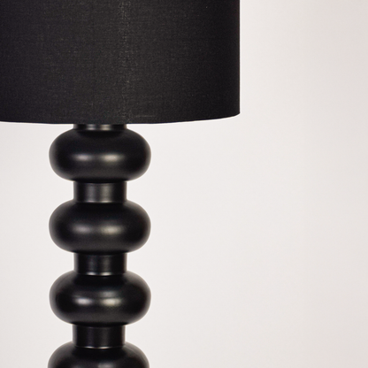 Closeup view of modern floor lamp showing textured black base stacked design and fabric shade detail with soft light highlighting craftsmanship and premium finish.