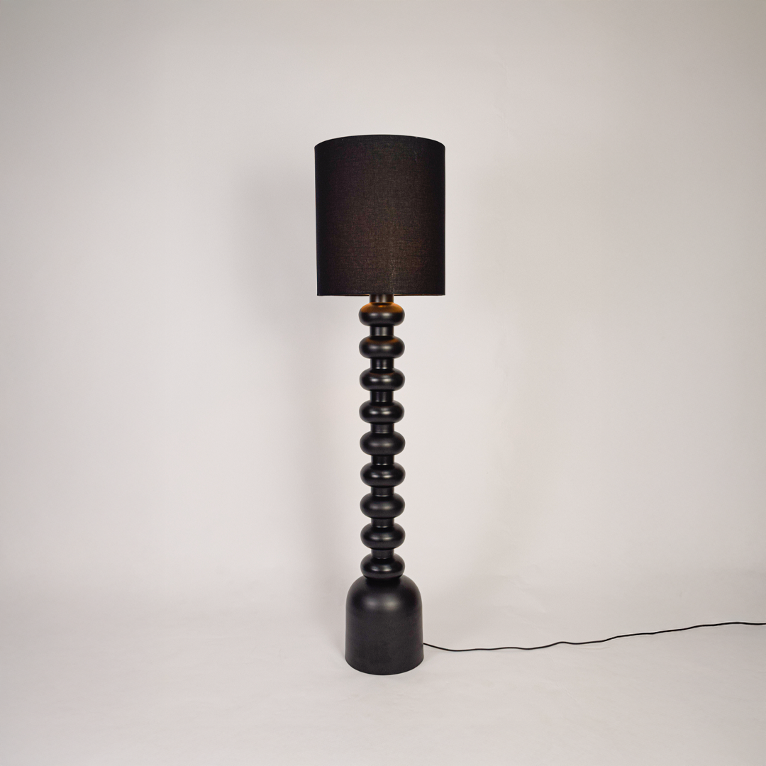 Floor lamp shown on clean white background with black sculpted base and tall fabric shade highlighting full height design and soft ambient lighting.