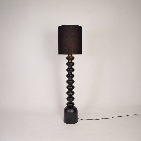 Floor lamp shown on clean white background with black sculpted base and tall fabric shade highlighting full height design and soft ambient lighting.