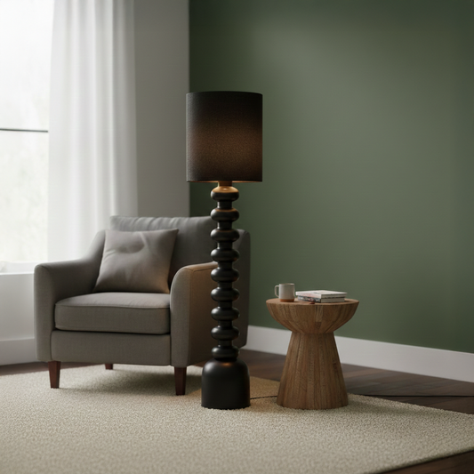 Floor lamp styled in a modern living room beside an armchair and wood side table showing warm glow with sculpted black base and soft fabric shade.