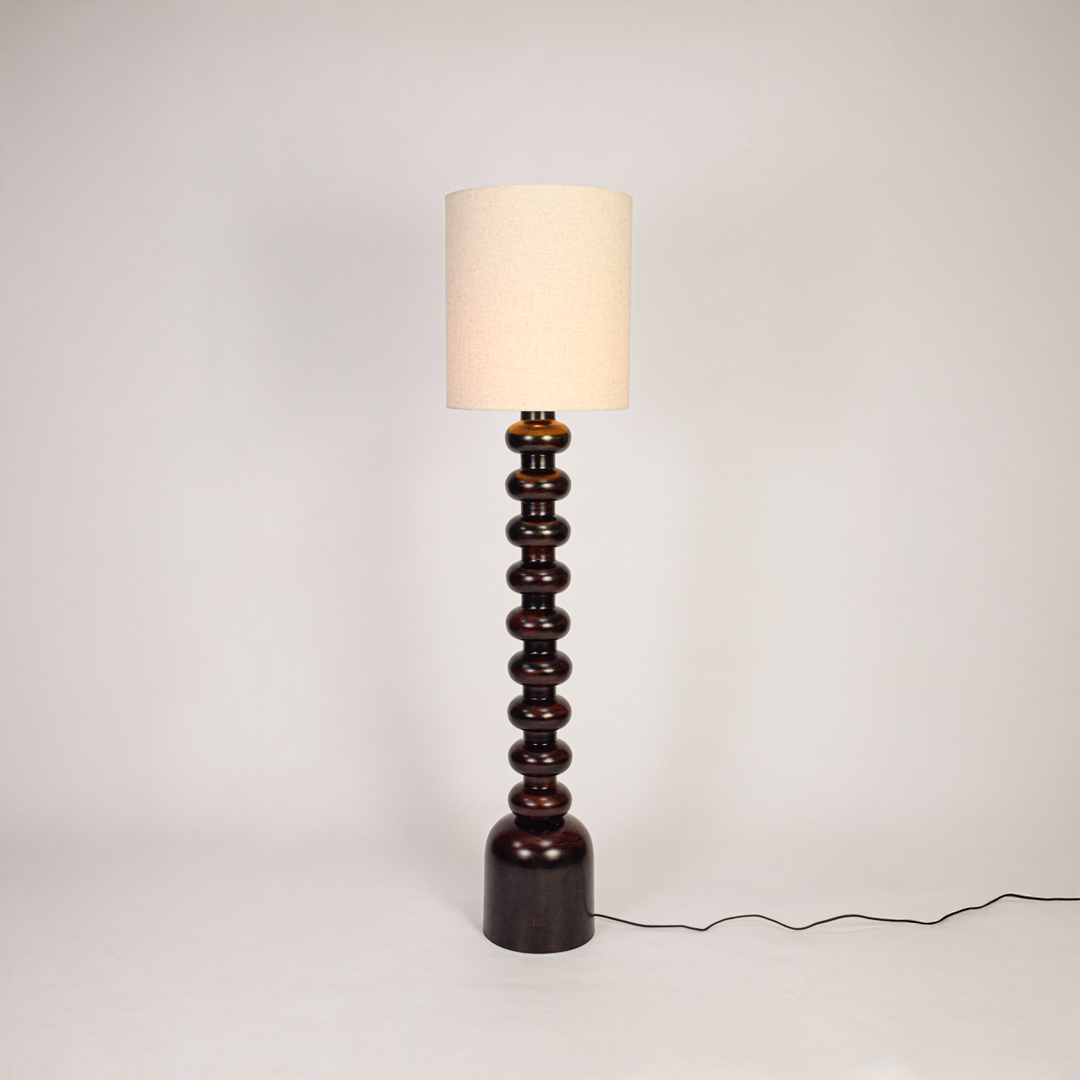 Floor lamp shown on clean white background with light on highlighting stacked sculpted base smooth finish and tall fabric shade for modern home decor.