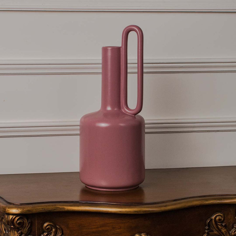 Contemporary pink ceramic vase photographed on a bright white backdrop emphasizing its smooth finish and sculptural handle design.